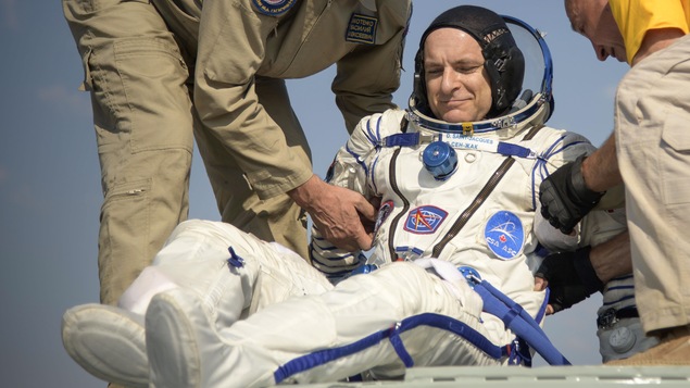 Deux hommes aident un astronaute à sortir d,une capsule spatiale.