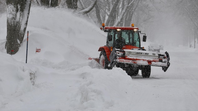 Un déneigeur à l'oeuvre avec son tracteur devant un banc de neige dans un quartier résidentiel
