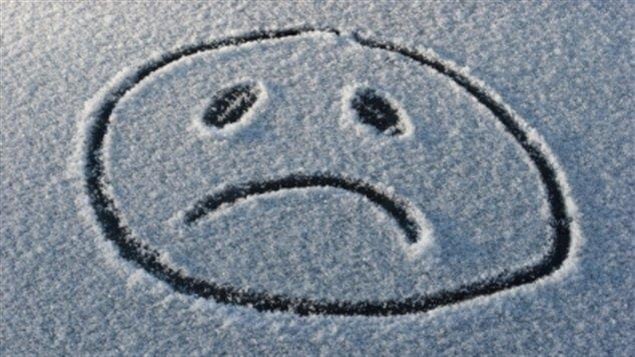 Le blues de l'hiver représenté par le dessin d'un visage triste dessiné dans la neige.
