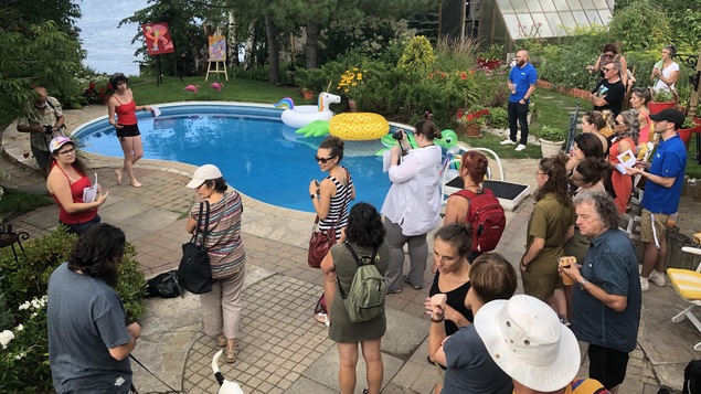 Des personnes écoutent une femme faire une présentation au bord d'une piscine creusée.
