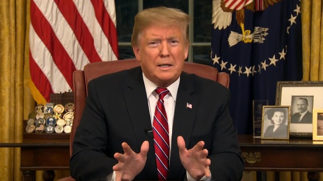 Donald Trump assis dans le bureau ovale, regardant la caméra.