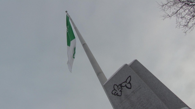 Le drapeau franco-ontarien flotte au-dessus d'un petit monument.