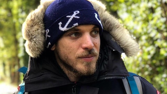 Un jeune garçon d'une vingtaine d'années habillé d'une doudoune et d'un bonnet.