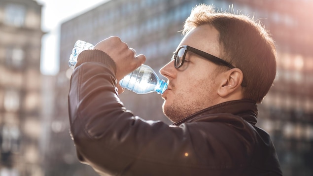 Un homme boit de l'eau dans une bouteille en plastique.
