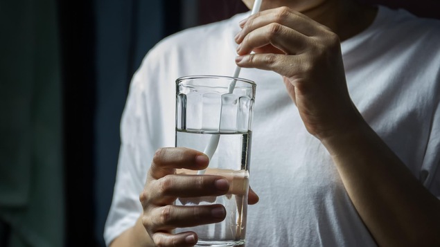 Une personne buvant de l'eau dans un verre à l'aide d'une paille.