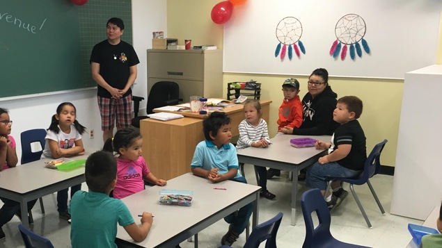L'enseignante de maternelle est debout devant les élèves assis aux trois tables de la classe.