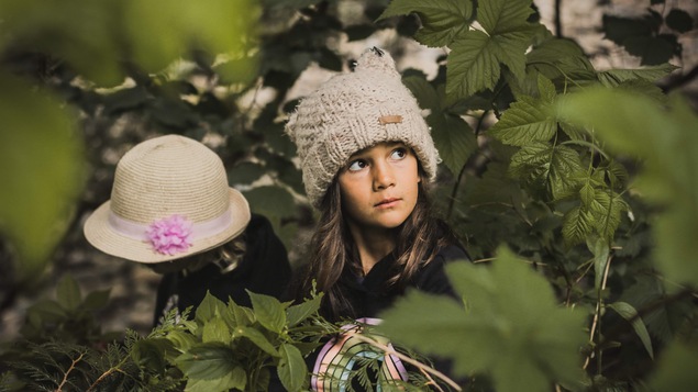 Deux enfants portant tuque et chapeau sont au milieu d'arbustes.