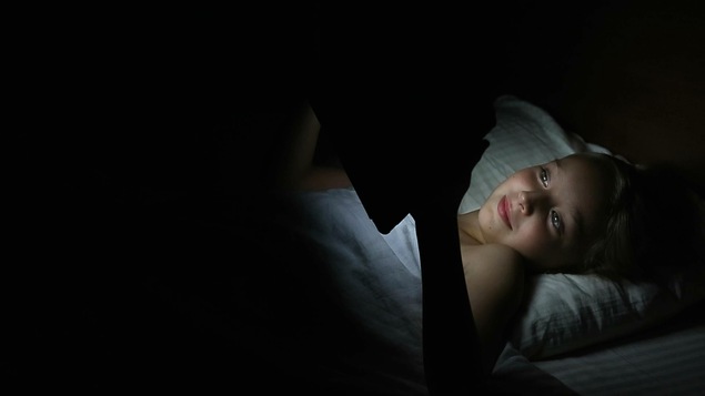 Une jeune fille consulte sa tablette avant de dormir.