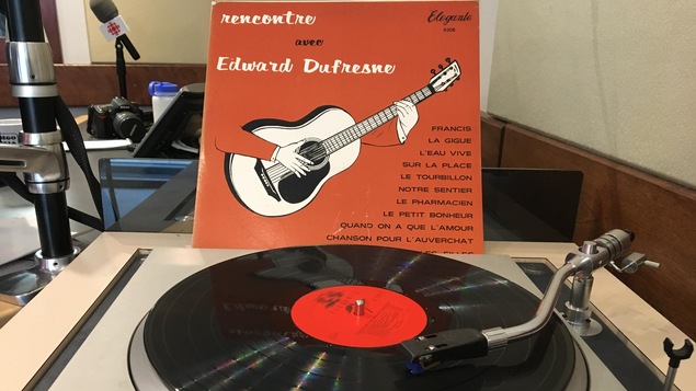 Une pochette de disque vinyle est appuyée sur une table tournante où se trouve le disque.