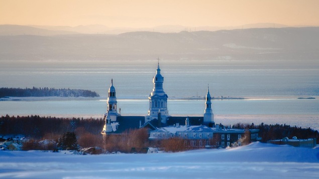 Point de vue sur une église qui se situe devant le fleuve Saint-Laurent, à Trois-Pistoles. On remarque les montagnes au loin qui trace une ligne d'horizon en hiver.