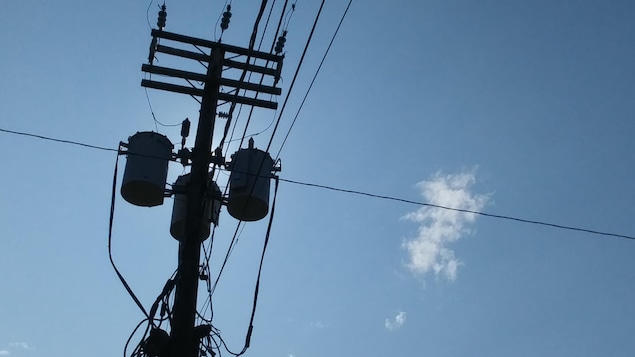 Une ligne électrique d'Hydro-Québec cache le soleil sous un ciel bleu.