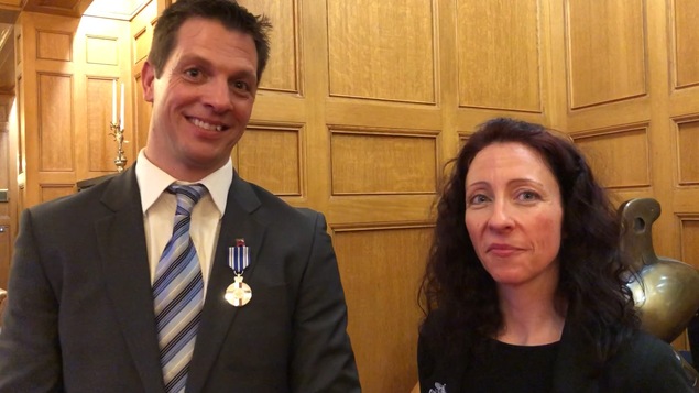Un homme et une femme posent avec leur médaille devant un mur de bois.