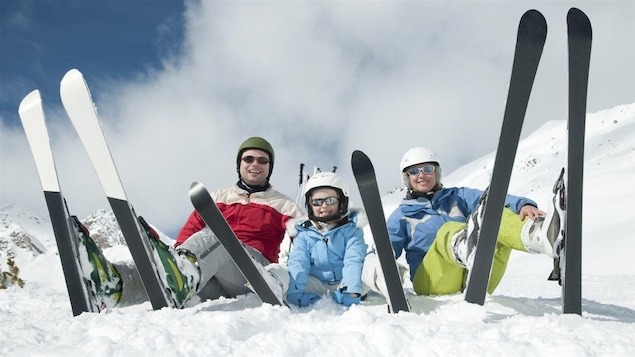 Une enfant et ses parents sont assis dans la neige avec des skis au pied.