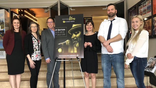 Quatre femmes et deux hommes posent de chaque côté d'une affiche du Festival blues Eldorado.