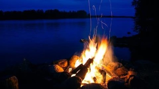 Feu de camp qui brûle à proximité d'un lac à la tombée du jour