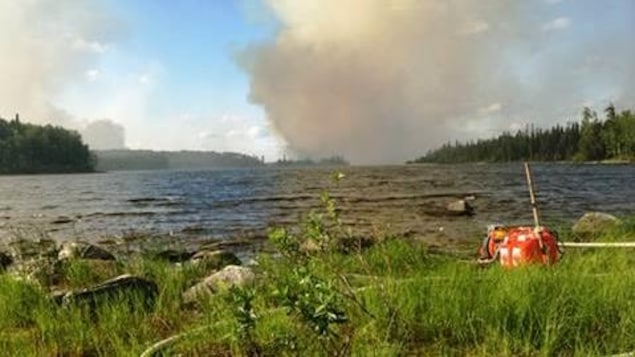 Le Nipigon District Fire Number 29, qui s'étend actuellement sur 1000 hectares, se trouve à une vingtaine de kilomètres au nord du territoire de la Première Nation Nibinamik. Sur la photo prise au bord d'un lac, on voit de la fumée dans le ciel. Le Nipigon District Fire Number 29, qui s'étend actuellement sur 1000 hectares, se trouve à une vingtaine de kilomètres au nord du territoire de la Première Nation Nibinamik. Sur la photo prise au bord d'un lac, on voit de la fumée dans le ciel.