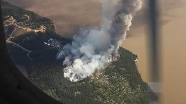 L'incendie Red Lake District Fire Number 066, près de la Première Nation de Sandy Lake, située dans le district de Kenora. Image prise d'un avion au dessus de la communauté. On y voit de la fumée près de bâtiments. L'incendie Red Lake District Fire Number 066, près de la Première Nation de Sandy Lake, située dans le district de Kenora. Image prise d'un avion au dessus de la communauté. On y voit de la fumée près de bâtiments.