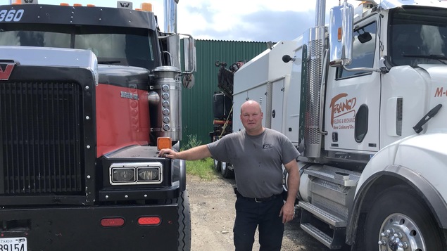 Un homme pose entre ses deux camions lourds de course.