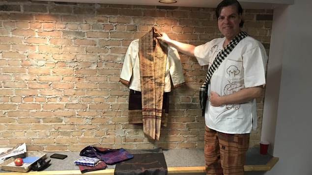 François Tremblay qui tient dans ses mains un costume traditionnel du Laos.