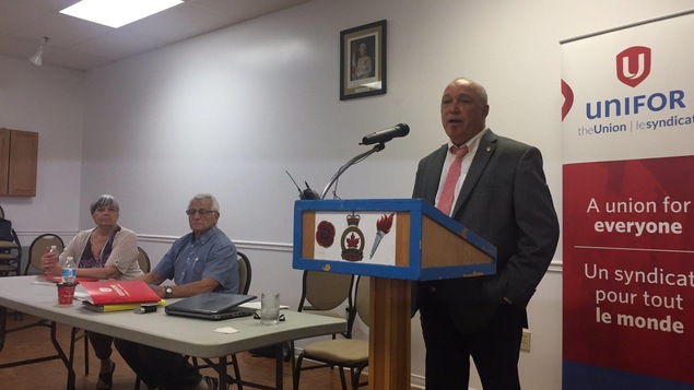 Trois personnes lors d'une présentation avec un panneau du syndicat Unifor Trois personnes lors d'une présentation avec un panneau du syndicat Unifor