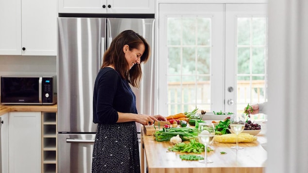 On voit la nutritionniste dans une cuisine aménagée. Elle coupe des légumes frais en souriant.