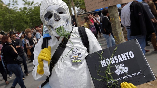 Un manifestant porte un masque de crâne et une affiche qui critique la compagnie Monsanto