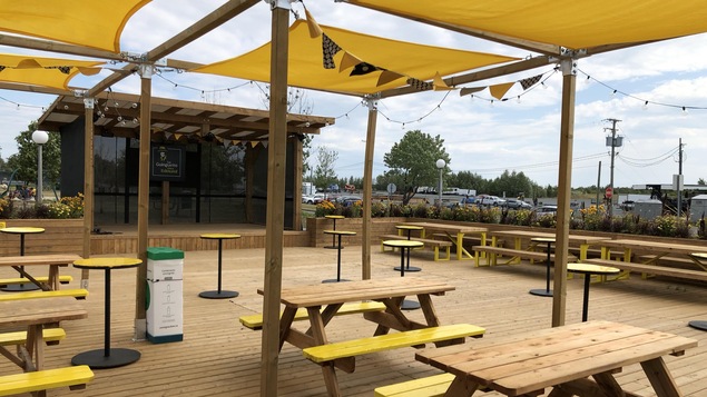 Une terrasse en bois avec des tables à pique-nique, des tables hautes et une scène.