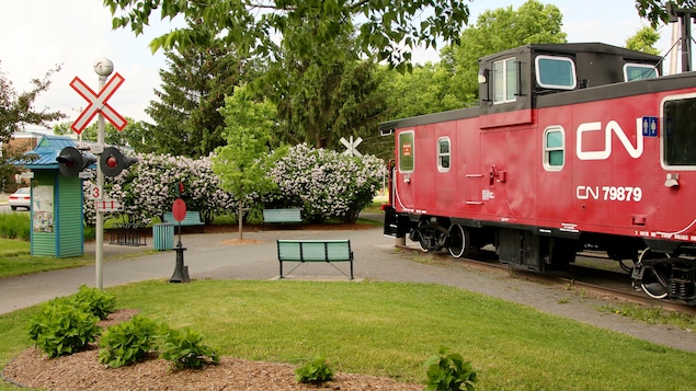 Un wagon de queue rouge du CN dans un jardin fleuri avec des bancs.