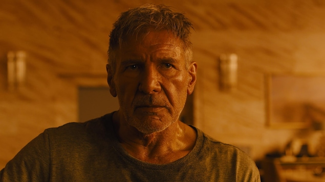 L'acteur Harrison Ford, dans une ambiance ambrée et sombre, dans le film Blade Runner 2049.