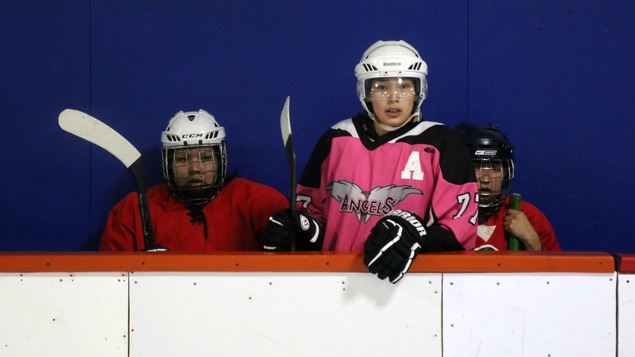 Des joueuses de hockey assises au banc de leur équipe observent un match, lors d’un tournoi de hockey autochtone à Val-d’Or.