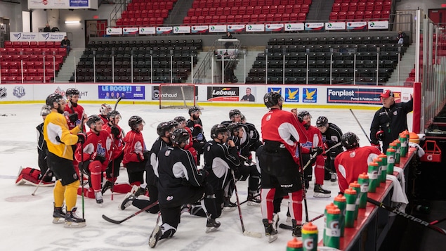 Les joueurs des Huskies se tiennent sur la patinoire devant leur entraîneur.