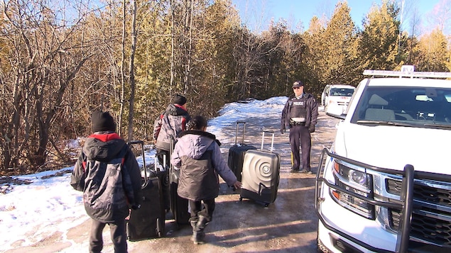 Des enfants, dont la famille a tenté d'entrer illégalement au Canada, marchent dans la neige en direction d'un policier. Des enfants, dont la famille a tenté d'entrer illégalement au Canada, marchent dans la neige en direction d'un policier.