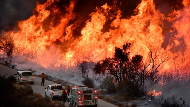 Des pompiers observent l'énorme brasier en bord de route.