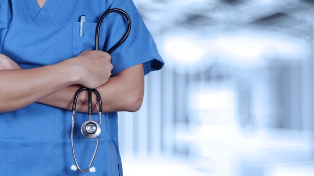 Un travailleur de la santé se tient les bras croisés avec un stéthoscope en main.