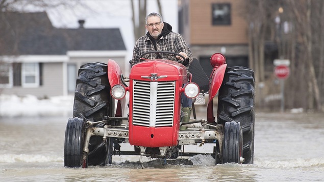 Un homme conduit un tracteur sur une rue inondée