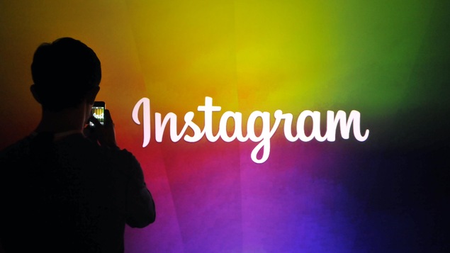 Un homme prend en photo le logo d'Instagram écrit en blanc sur un mur multicolore.