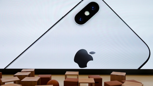 Une photo montrant un écran sur lequel est affiché un iPhone X et devant lequel sont disposés des tabourets cubiques et des ballons.