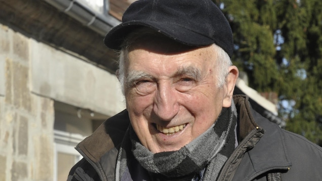 Un homme souriant avec une casquette à l'extérieur devant une maison.