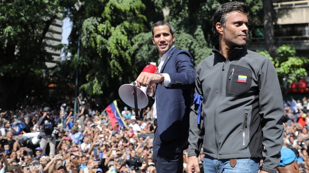 Deux hommes souriant, debout sur une plateforme, au milieu d'une foule, à l'extérieur.