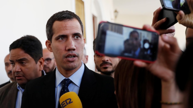 Juan Guaido parle dans un micro jaune d'une journaliste, il est en costume sombre et porte une cravate à pois.