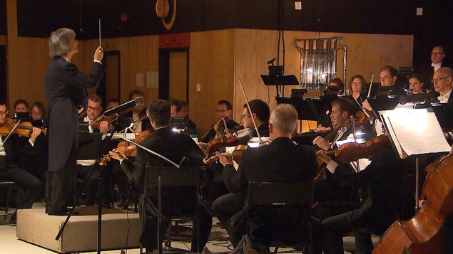 Kent Nagano dirige un orchestre dans la salle Teueikan de Maliotenam