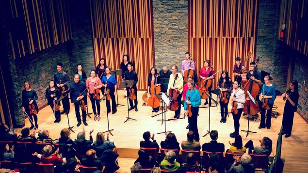 Un orchestre de chambre à cordes reçoit les applaudissements du public.