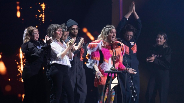 Une chanteuse et son groupe se réjouissent sur scène après avoir reçu un trophée. 