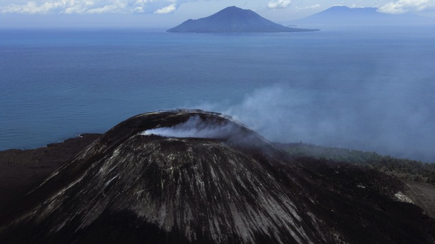 Une vue aérienne montre un cratère de volcan qui fume. Il est situé sur une île.