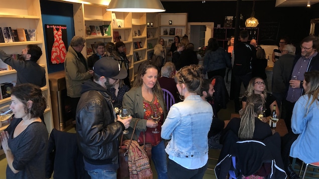Des gens discutent en tenant des coupes de vin dans une librairie.