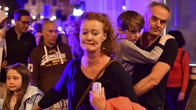 Des hommes et des femmes tenant leurs enfants quittent rapidement un lieu la nuit. Ils semblent légèrement paniqués et ont les yeux écarquillés
