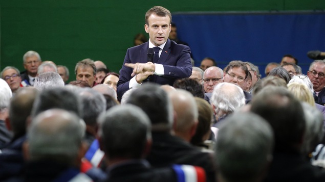 Un homme parle au micro, debout au milieu d'une assemblée principalement masculine.