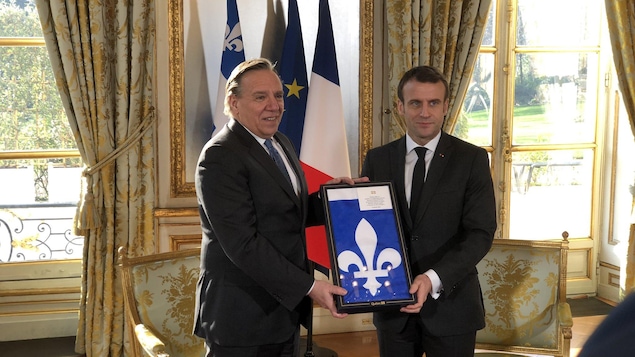 François Legault et Emmanuel Macron tiennent un drapeau du Québec encadré.