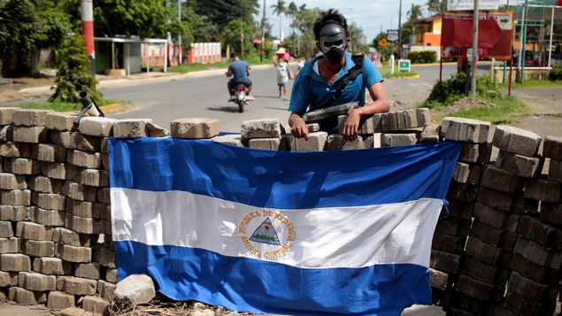 Un manifestant masqué pose devant un drapeau du Nicaragua.