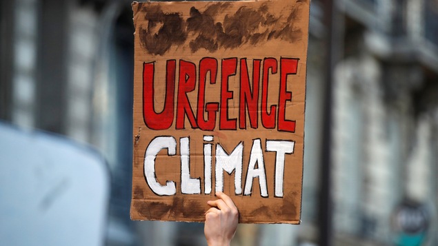 Une personne tient une pancarte sur laquelle on peut lire : « Urgence climat ».